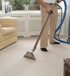 Professional carpet cleaner using a hot-water extraction wand and hose machine in a living room in Memphis, TN.