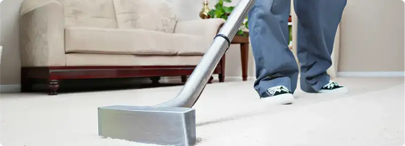 Carpet cleaning technician using a hot-water extraction wand on a light-colored carpet in a living room, Memphis, TN.