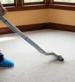 Steam carpet cleaning technician using a hot-water extraction wand on a residential carpet, wearing blue protective shoe covers Memphis, TN.