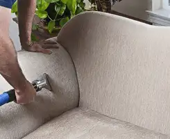 Professional upholstery cleaner deep-cleaning a fabric sofa with a handheld extraction tool and hose in Memphis, TN.